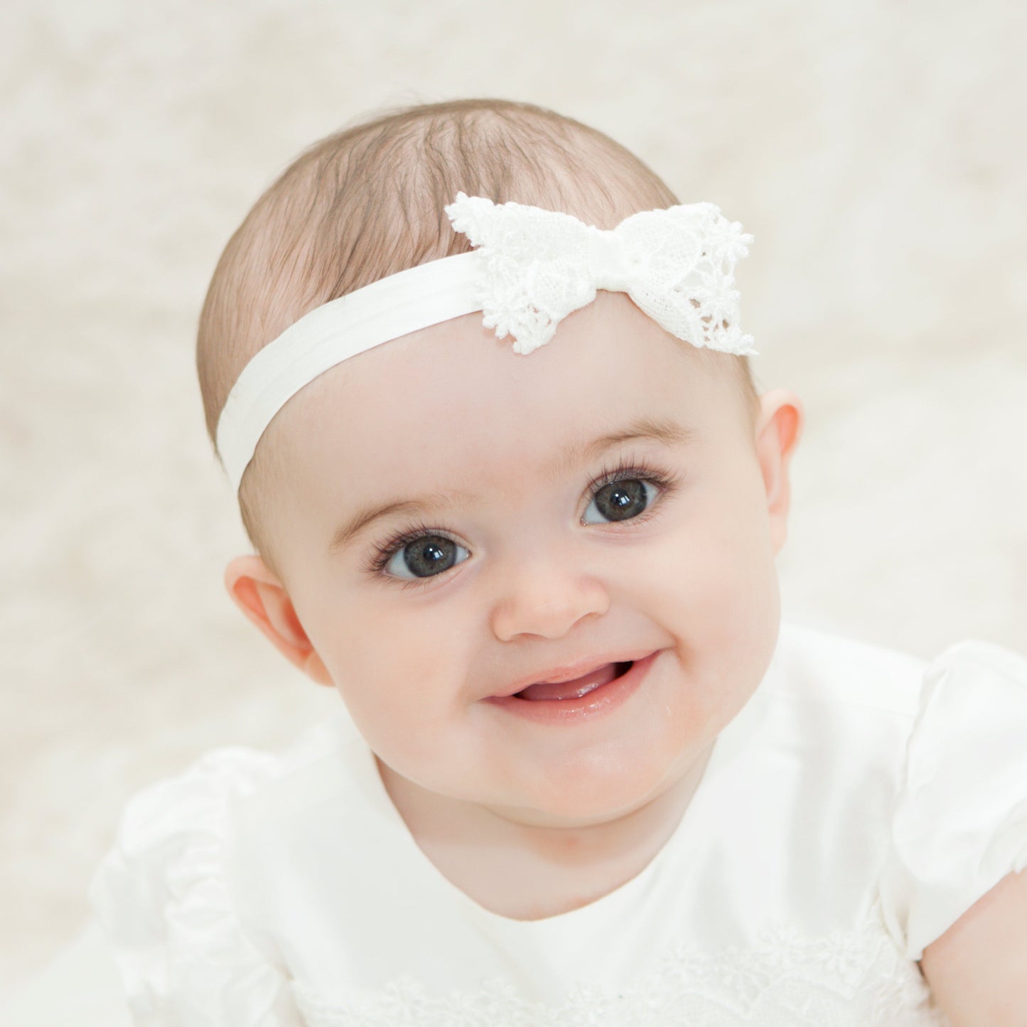 A smiling baby wearing the ivory silk and lace special occasion baby headband
