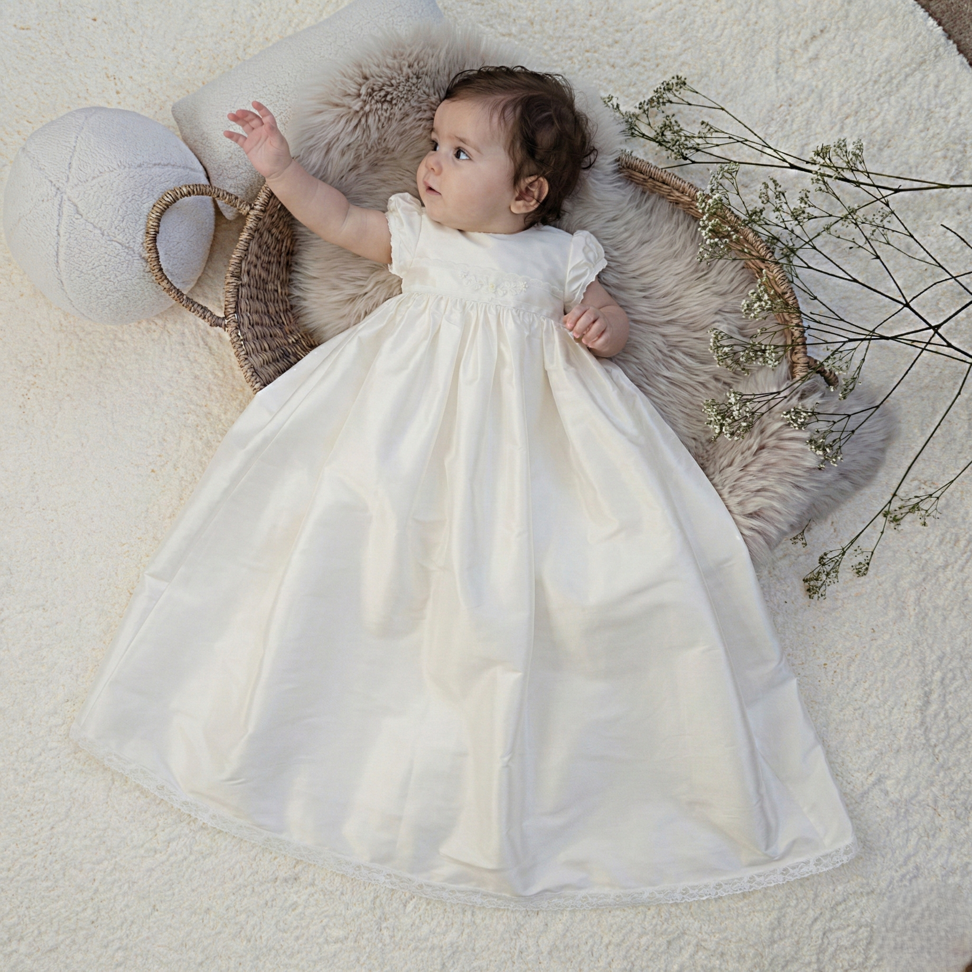 Baby in an ivory christening gown lying on a soft surface with decorative elements