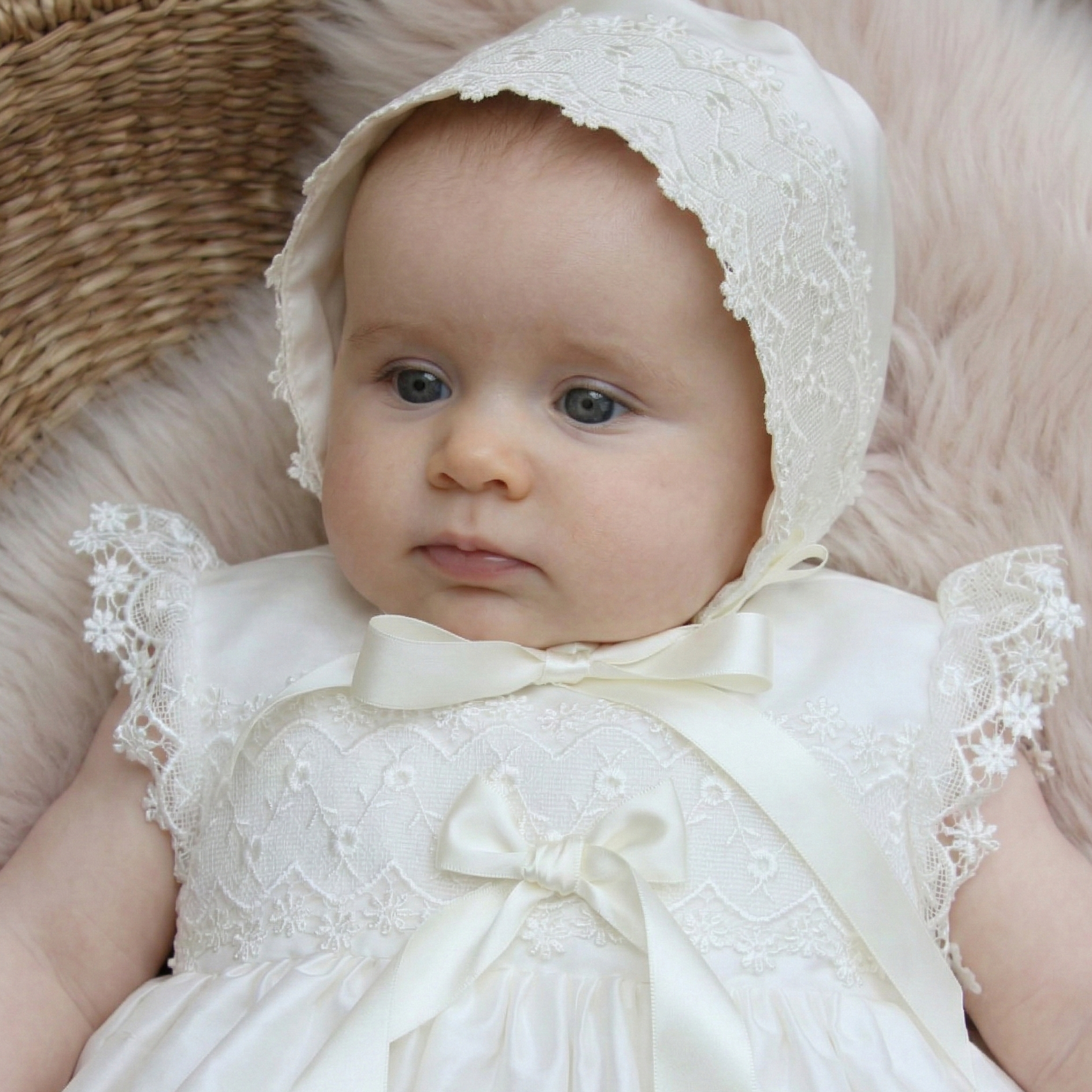 Baby in a white lace dress and bonnet lying on a soft surface