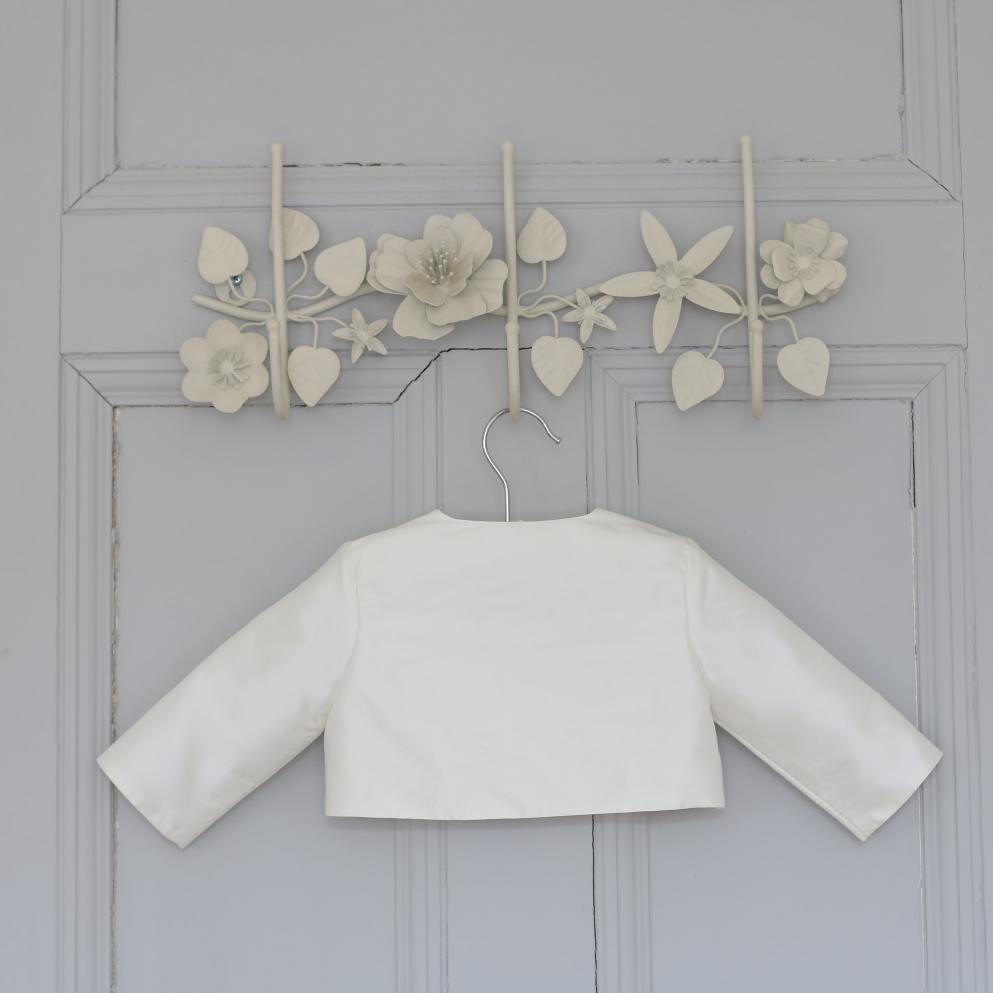Back view of the James baby boy christening jacket shown hanging on a doore
