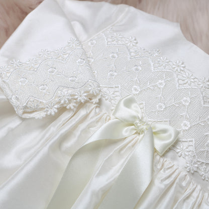 Close-up of the ivory silk Lara baby dress with delicate floral lace applique and a matching satin bow at the waist.