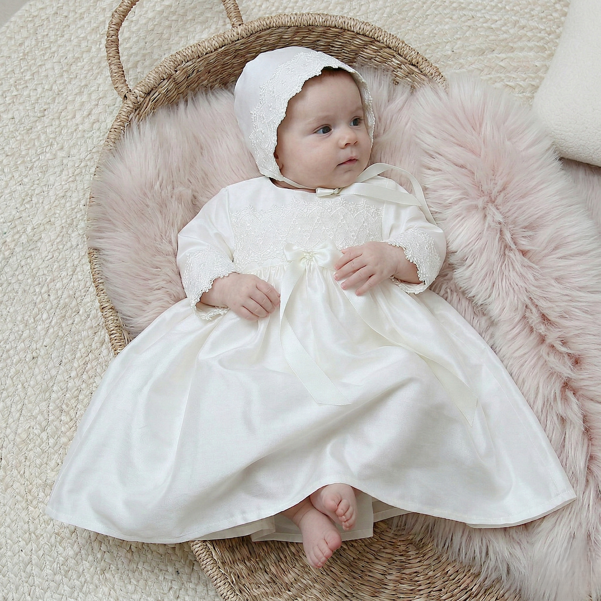 Lara long sleeved christening dress in ivory silk with lace trim shown on a baby wearing the matching bonnet