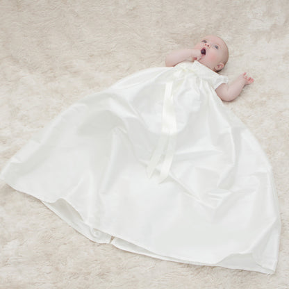 baby lying on a carpet wearing the full length Lily baptism gown in ivory