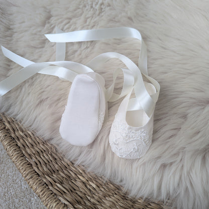 Ivory Lucy baptism ballet shoes with ribbons on a fluffy white surface