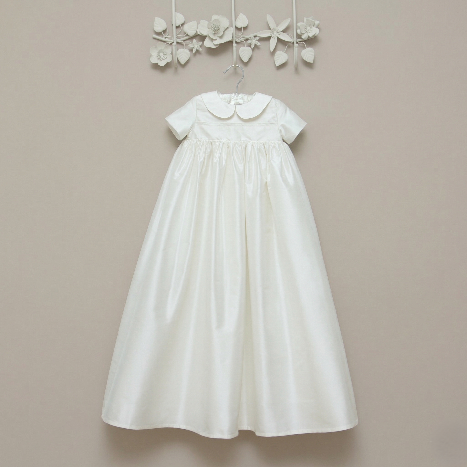 Luke silk christening gown hanging on a wall. Shown in ivory with short sleeves