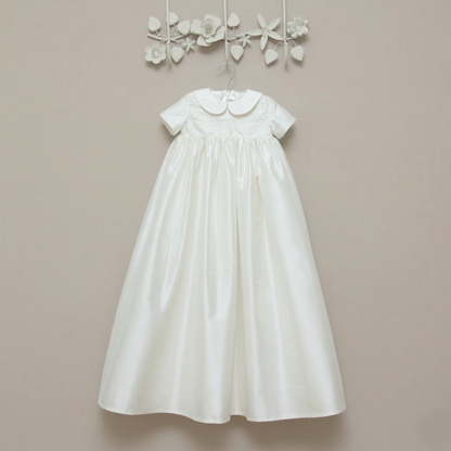 Luke silk christening gown hanging on a wall. Shown in ivory with short sleeves