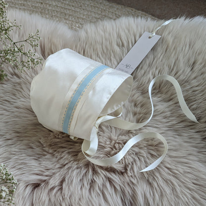White baby bonnet with blue ribbon on a fluffy white surface with baby's breath flowers.