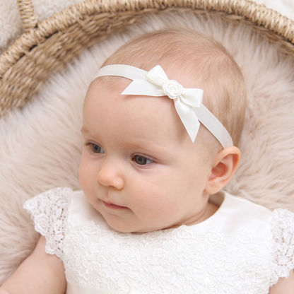 Close-up of a baby wearing a Mila & Moss white Rachel silk headband with a satin ribbon bow, paired with a matching ivory Rachel dress