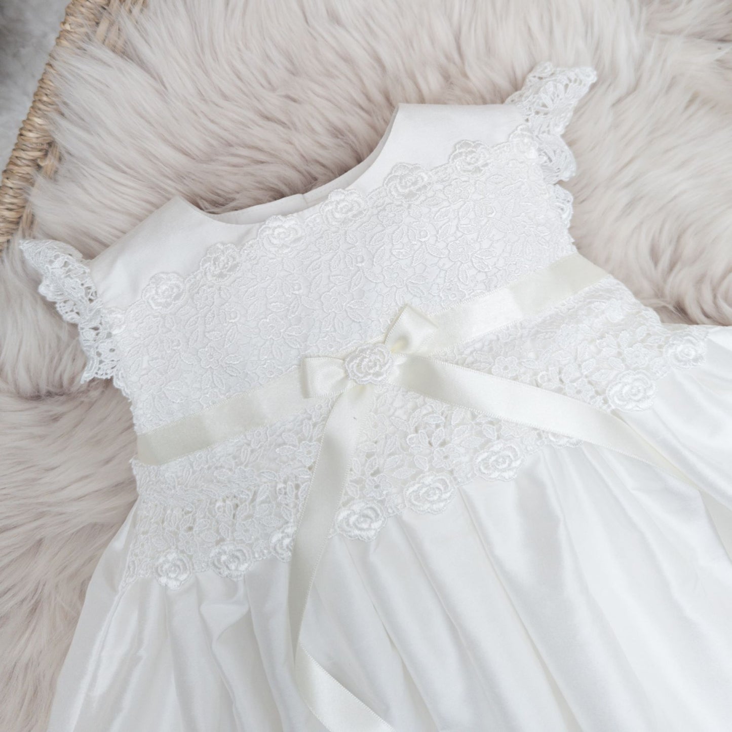 Close-up macro shot of the delicate lace detailing and fine craftsmanship on the ivory Rachel silk christening dress.