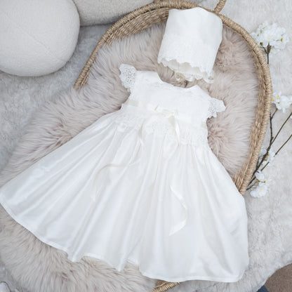 Front view of the ivory Rachel silk christening dress, styled with the optional matching silk bonnet