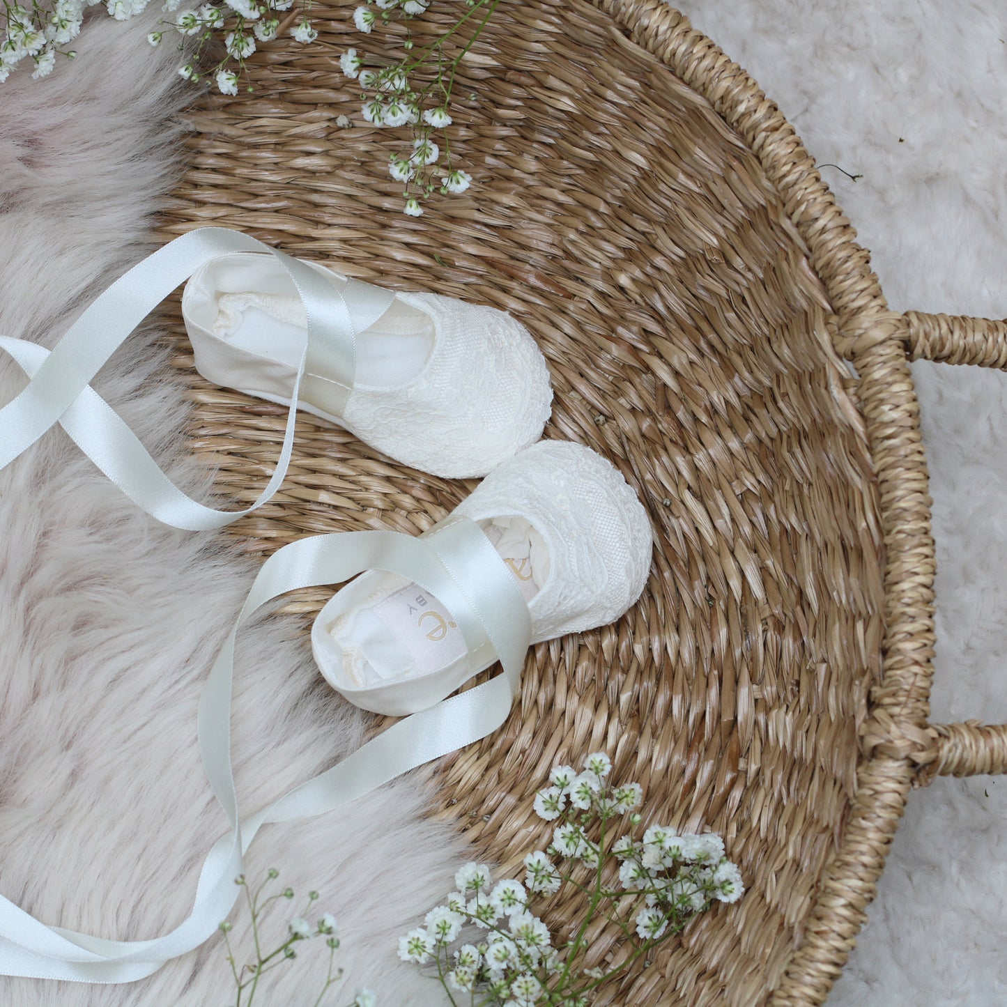 A pair of baby baptism booties in the Scarlett style shown in a basket with little flowers beside