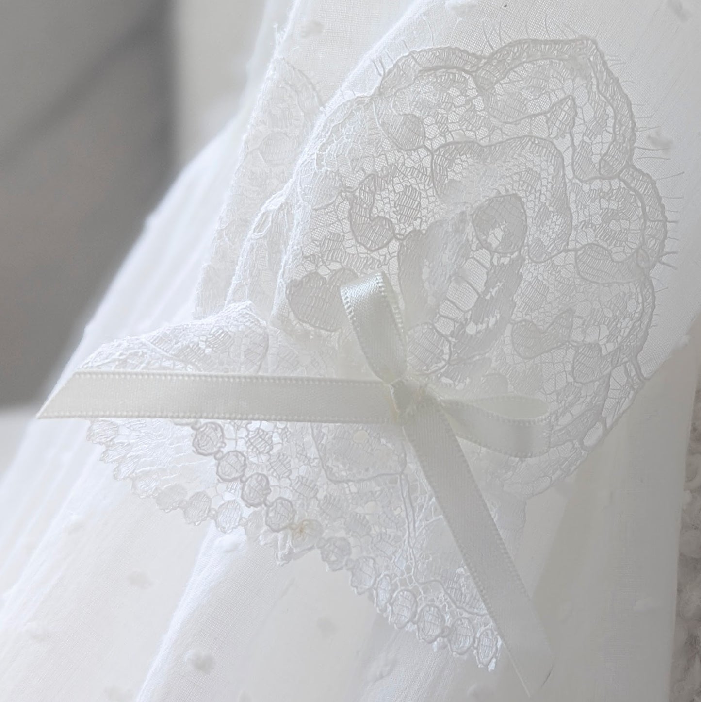 Close-up of the elegant long sleeves on the Isabella christening gown, featuring fine French lace-trimmed cuffs and a delicate handmade bow.
