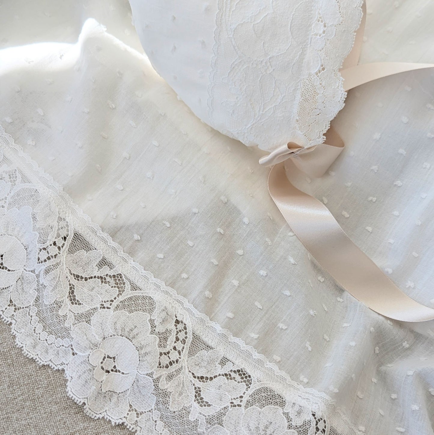 The draped hemline of the long Eliana baptism gown, showcasing the intricate wide French lace.