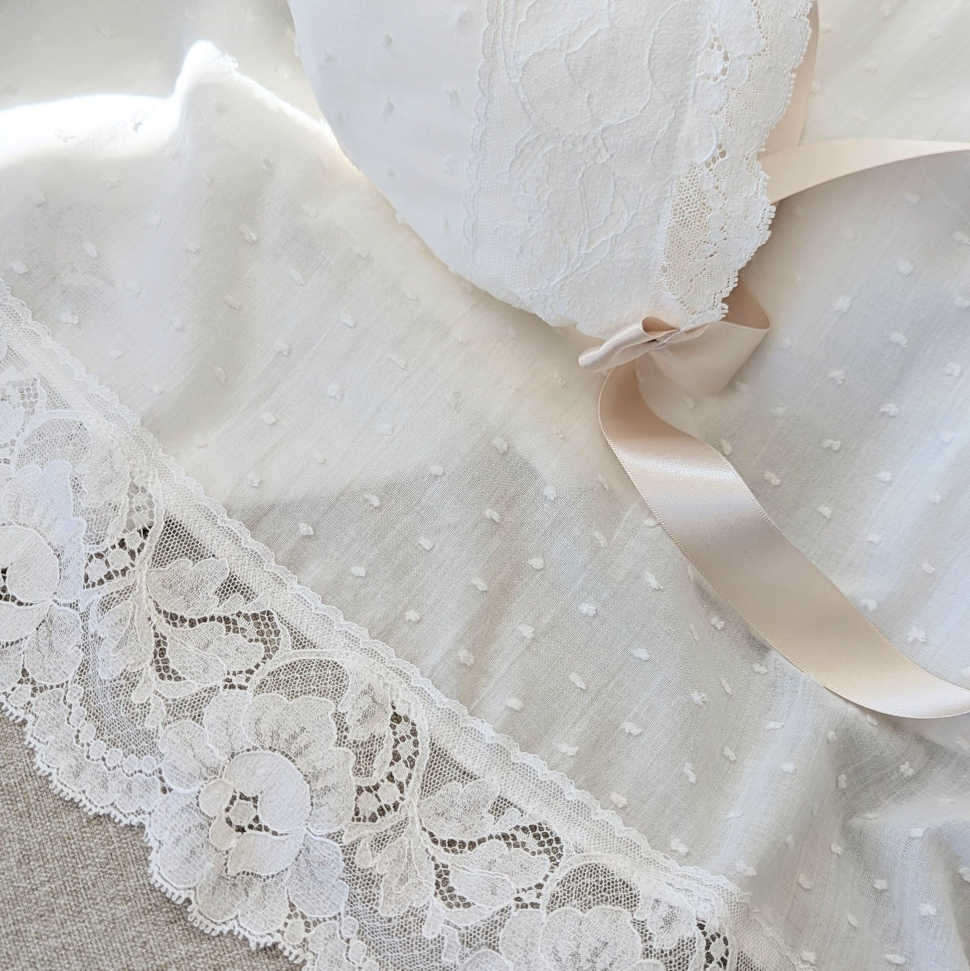 The draped hemline of the long Eliana baptism gown, showcasing the intricate wide French lace.